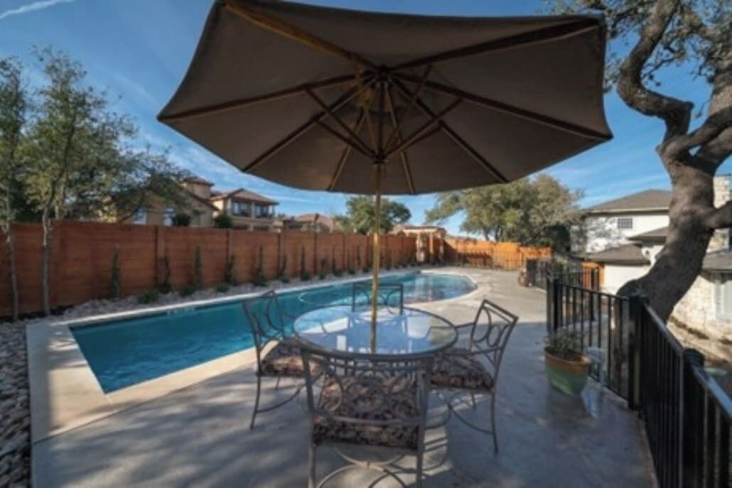 A poolside area with a round table and chairs, an umbrella, and a pool.
