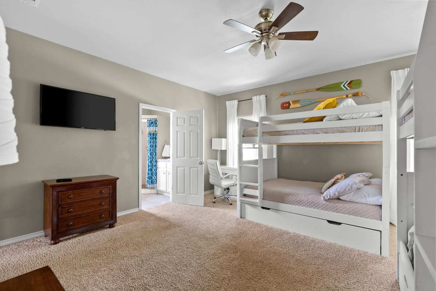 Un dormitorio con literas, ventilador de techo, televisión, cómoda de madera y escritorio con silla.