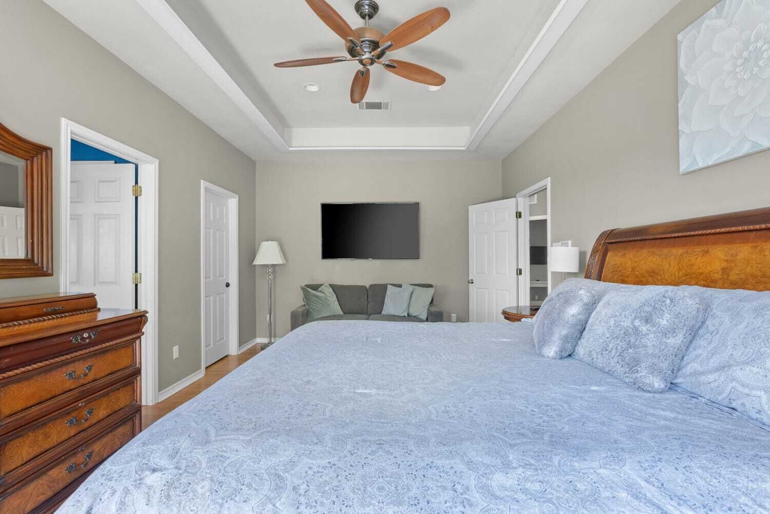 A bedroom with a large bed, a ceiling fan, a dresser, a TV, and a closet.