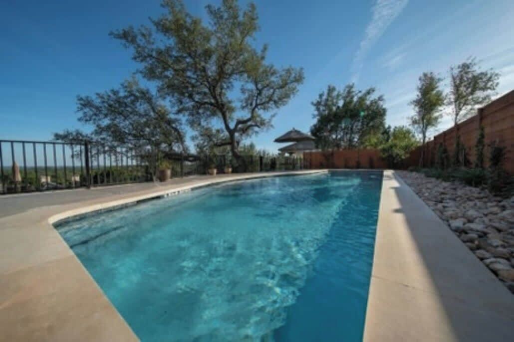 Una piscina de borde curvo, rodeada por un deck de concreto y una cerca de metal.