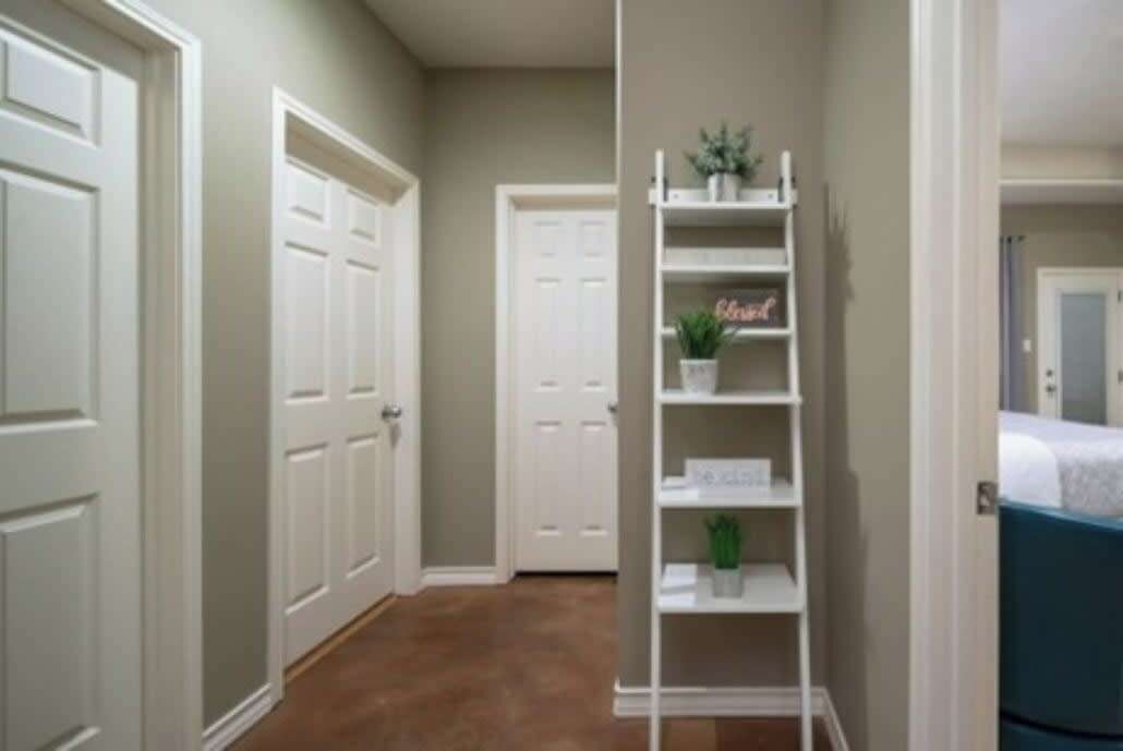 A hallway with white doors, a white shelving unit with a sign, and a blue bed in the background.