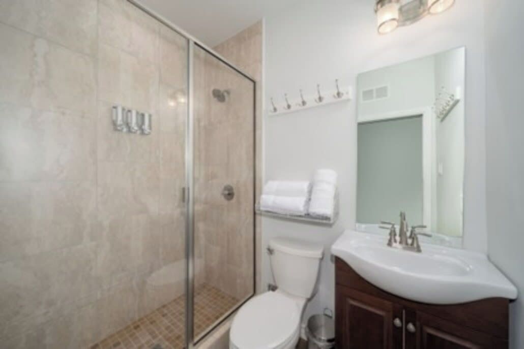 A modern bathroom with a glass-enclosed shower, a white toilet, and a vanity with a mirror.