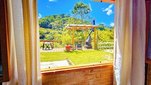 A view from a window of a room with a wooden structure outside, a grassy area, and a hill in the background.
