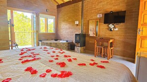 A room with a bed covered in rose petals, a stone fireplace, a television, and a wooden door labeled "Prime".