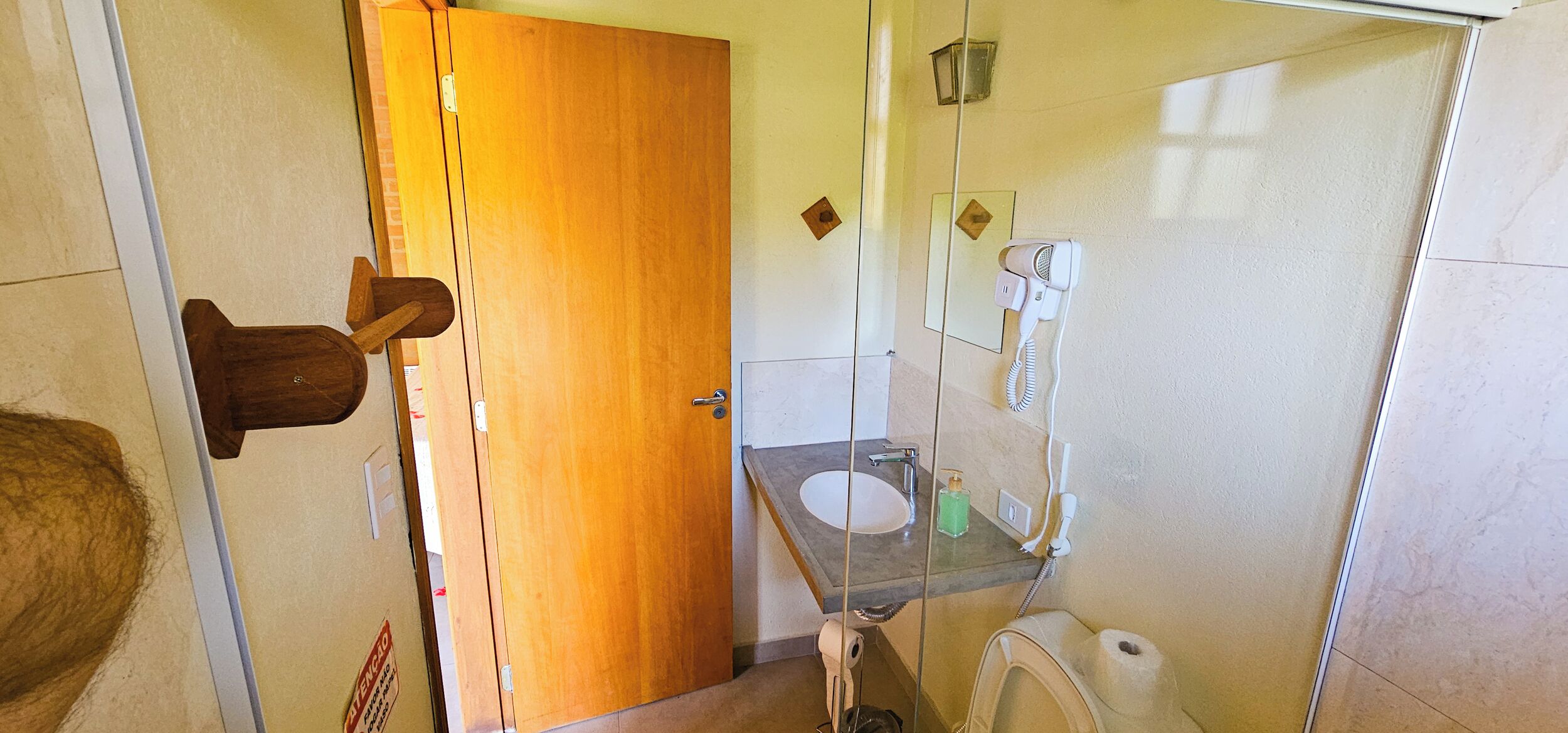 Une salle de bain avec une porte en bois, une cabine de douche en verre, un lavabo avec un miroir et des toilettes.