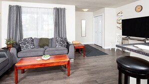 Een moderne woonkamer met een grijze bank, een houten salontafel en een flatscreen televisie.