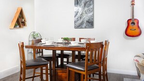 Een eetgedeelte met een houten tafel voor vier personen, omringd door stoelen. Een gitaar hangt aan de rechterkant van de muur.
