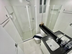 Un baño moderno con ducha acristalada, inodoro blanco y encimera negra con lavabo y artículos de aseo.
