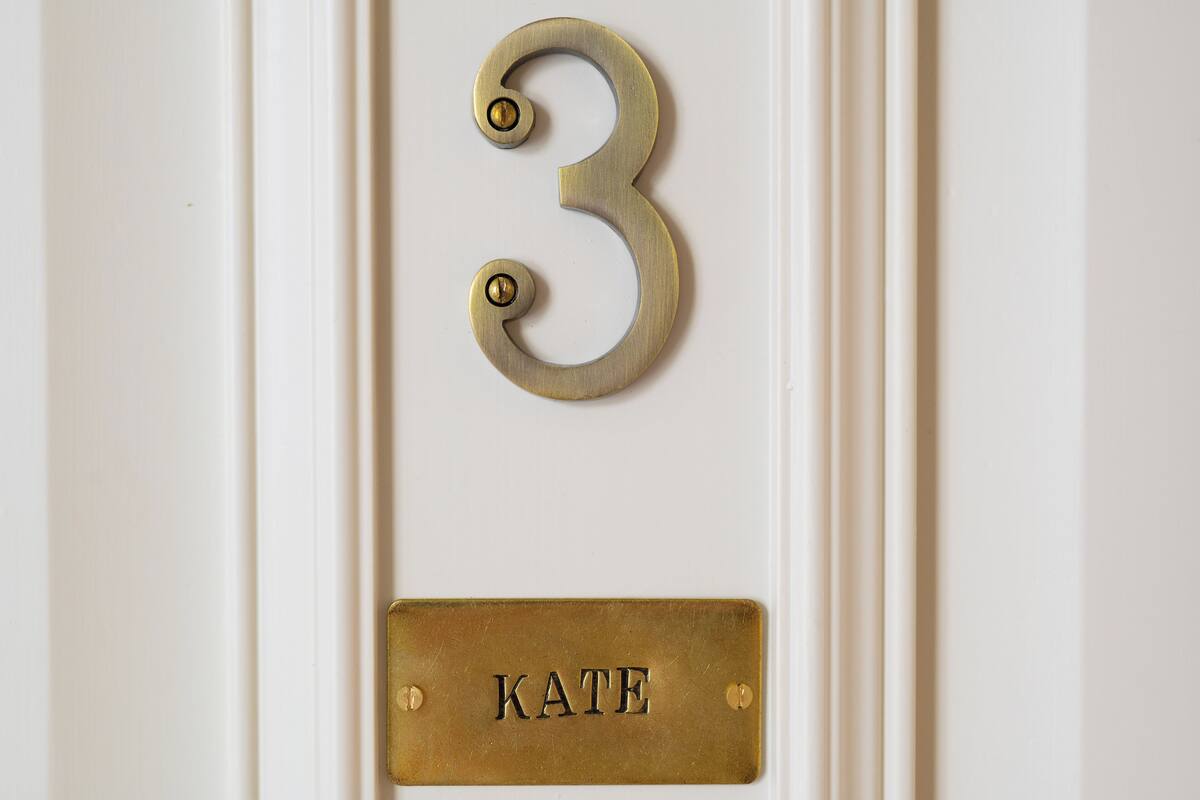 A brass number 3 and a brass nameplate with the name "KATE" on a white door.