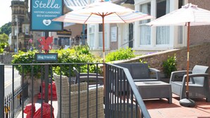 An outdoor seating area with wicker furniture and striped umbrellas, a 'dog friendly' sign, and a historic building in the background. - The Stella Historic Llandudno B&B (Llandudno)