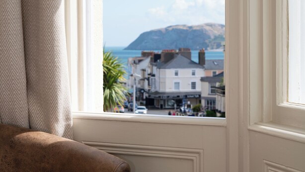 A room with a view of a coastal town, a brown leather chair, and a small table with white cups and a teapot. - The Stella Historic Llandudno B&B (Llandudno)