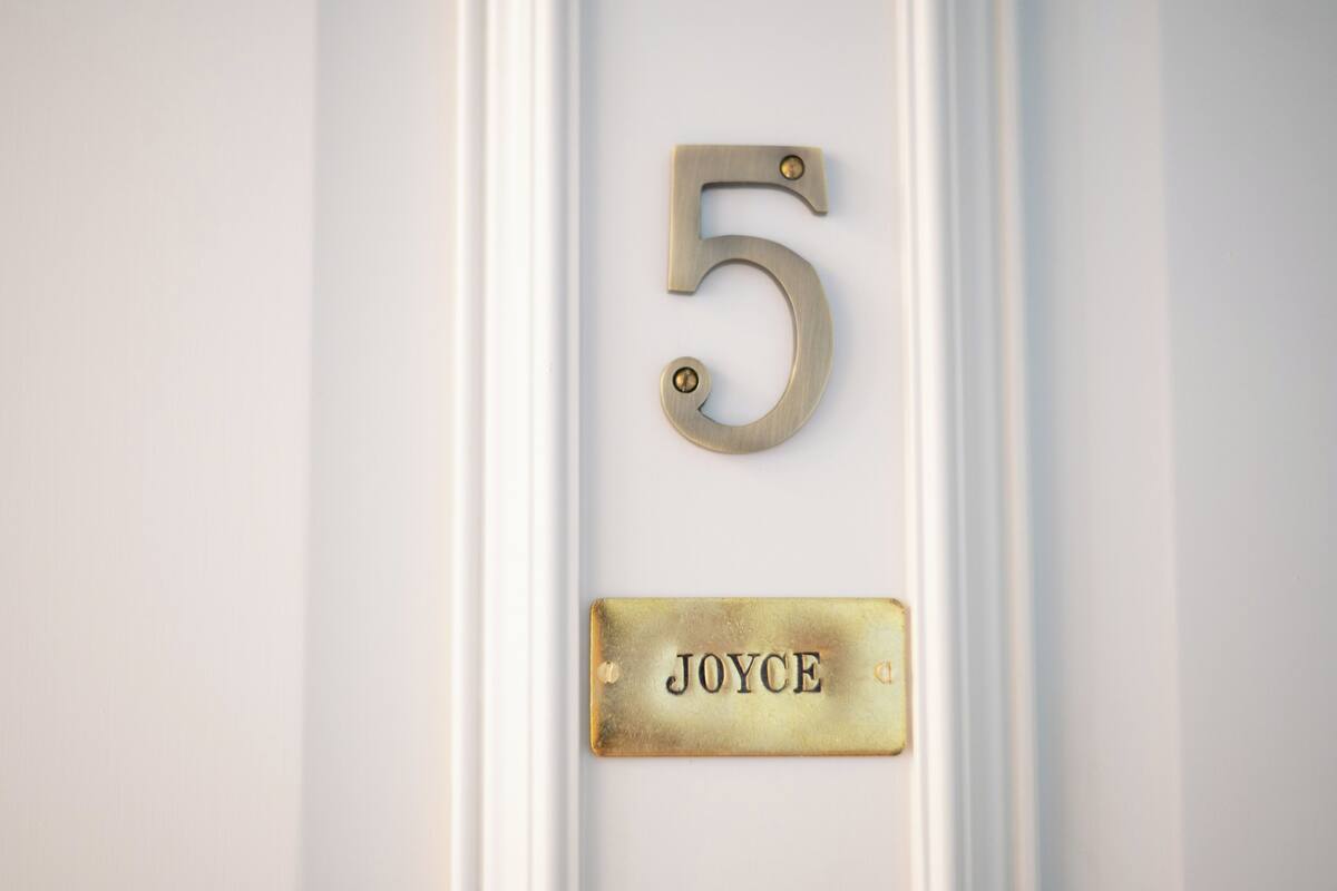 A brass number '5' and a nameplate with the name 'JOYCE' on a white door.