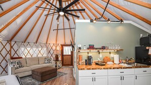 Interior acogedor de una yurta con sala de estar, kitchenette y ventilador de techo.
