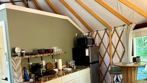 Cocina compacta con armarios blancos, un refrigerador negro y un microondas encima. Hay una mesa de madera con dos taburetes y un tapete estampado en el suelo.