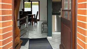 Un corridoio con una scala in legno, un tappeto nero, una zona pranzo con sedie e tavolo, e una cucina con frigorifero.