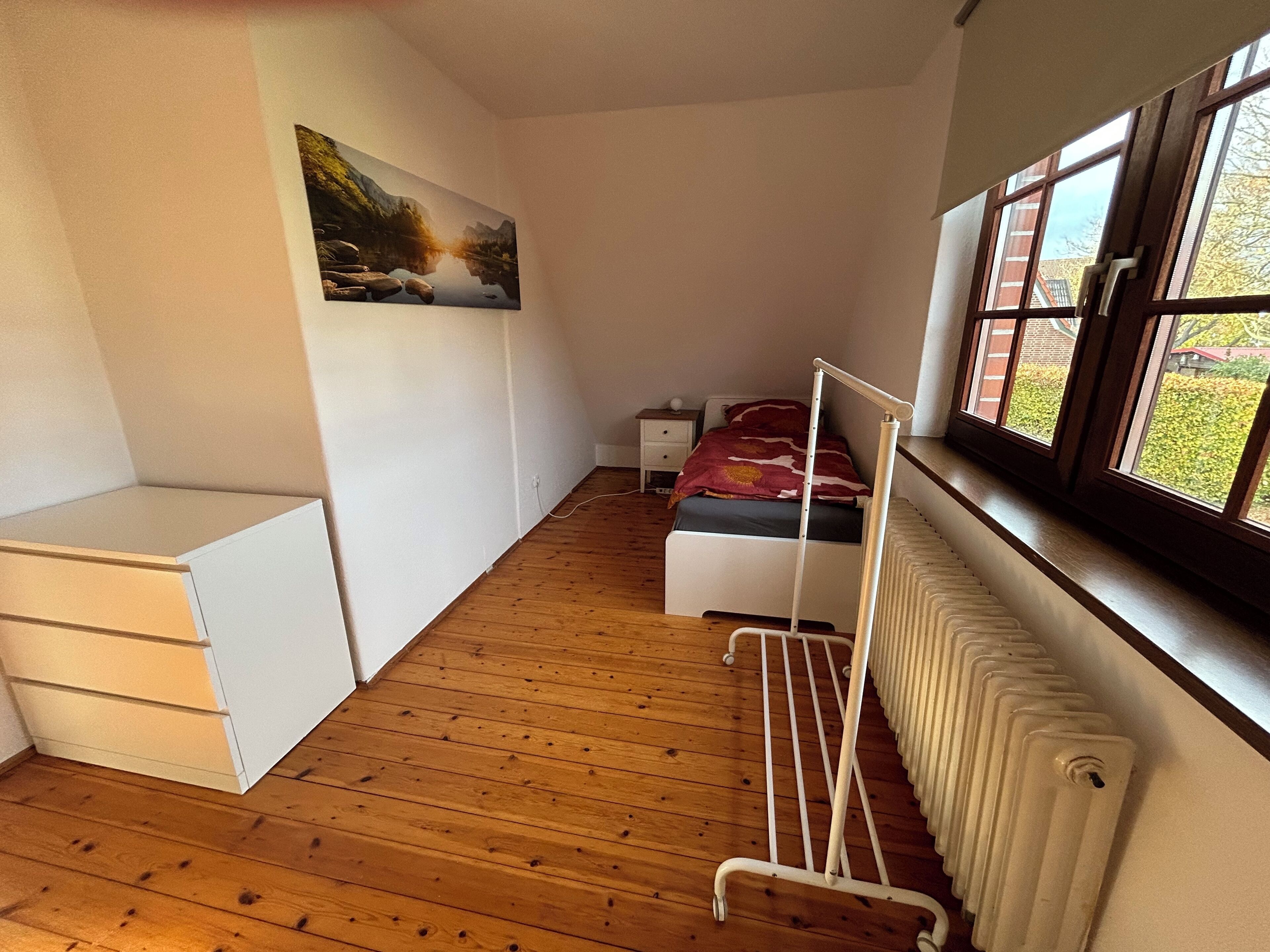 Ein Schlafzimmer mit einem Bett, einem Heizkörper, einem Fenster mit Blick und einem kleinen Nachttisch.