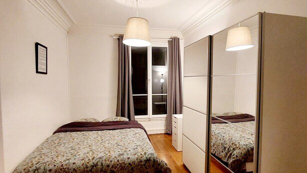 A bedroom with a bed, a wardrobe, and a window with curtains. - Large, charming apartment near Montparnasse (Paris)