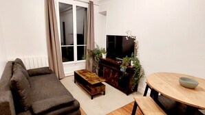A living room with a sofa, a coffee table, a TV stand with plants, and a dining table with chairs. - Large, charming apartment near Montparnasse (Paris)