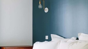 A bedroom with a bed, white bedding, a wooden nightstand, and a wall-mounted light fixture. - Charming quiet apartment in the heart of Paris (Paris)
