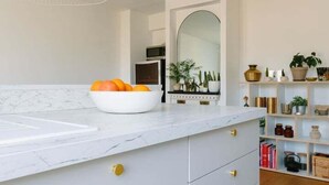 A modern kitchen with a marble countertop, a bowl of oranges, and a white cabinet with gold handles. - Charming quiet apartment in the heart of Paris (Paris)