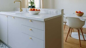 A modern kitchen with a white countertop, a gold faucet, and a bowl of fruit. - Charming quiet apartment in the heart of Paris (Paris)