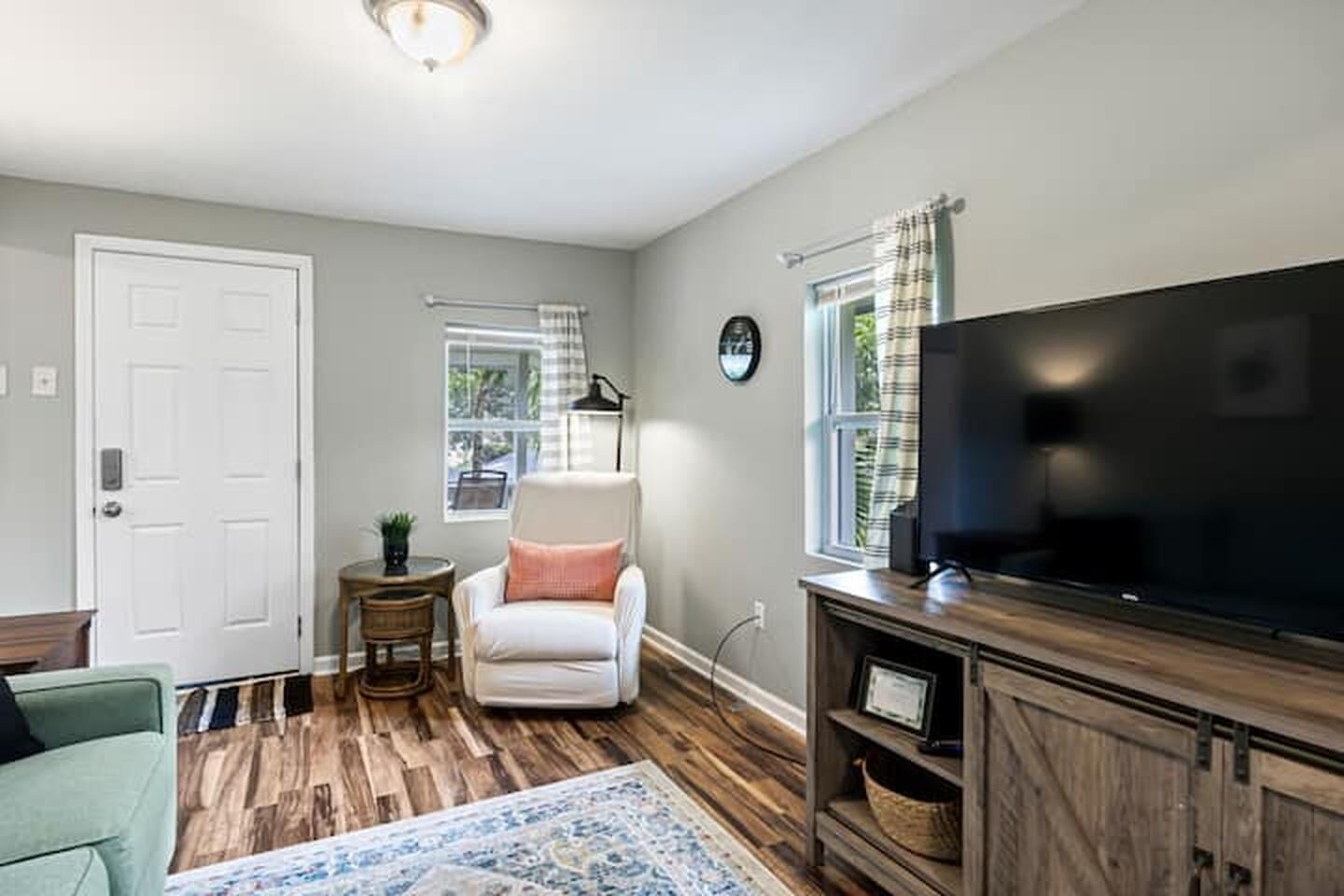 A living room with a white armchair, a television, a wooden entertainment unit, and a patterned rug.