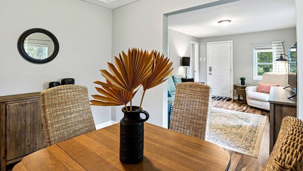 Un coin repas avec une table en bois, des chaises en osier et un vase noir contenant des plantes séchées.