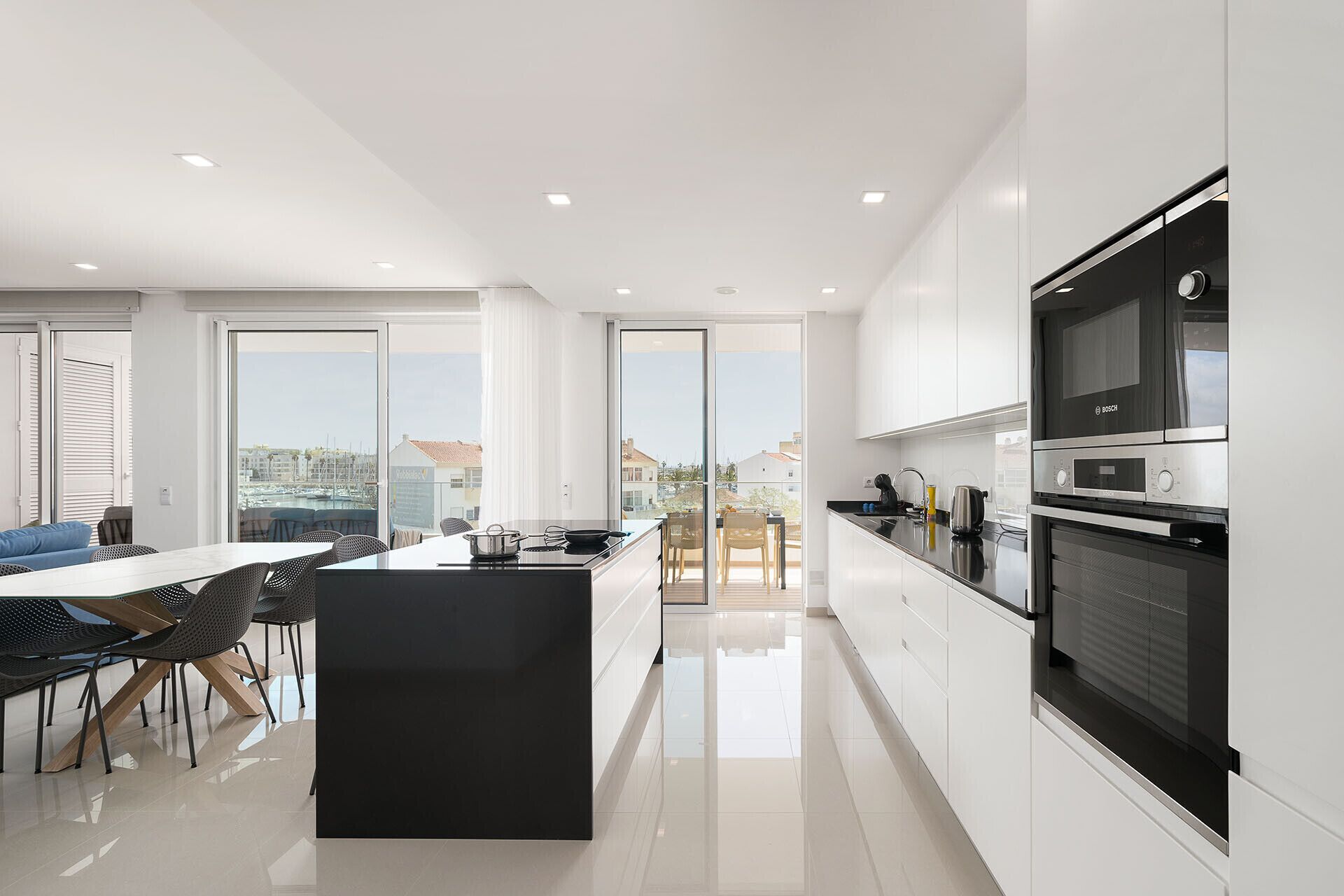 Une cuisine moderne dotée d’un grand îlot central, d’un coin repas avec des chaises et offrant une vue sur la ville grâce à de grandes fenêtres.