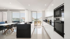 Una cocina moderna con una isla grande, un comedor con sillas y vistas a la ciudad a través de amplios ventanales.