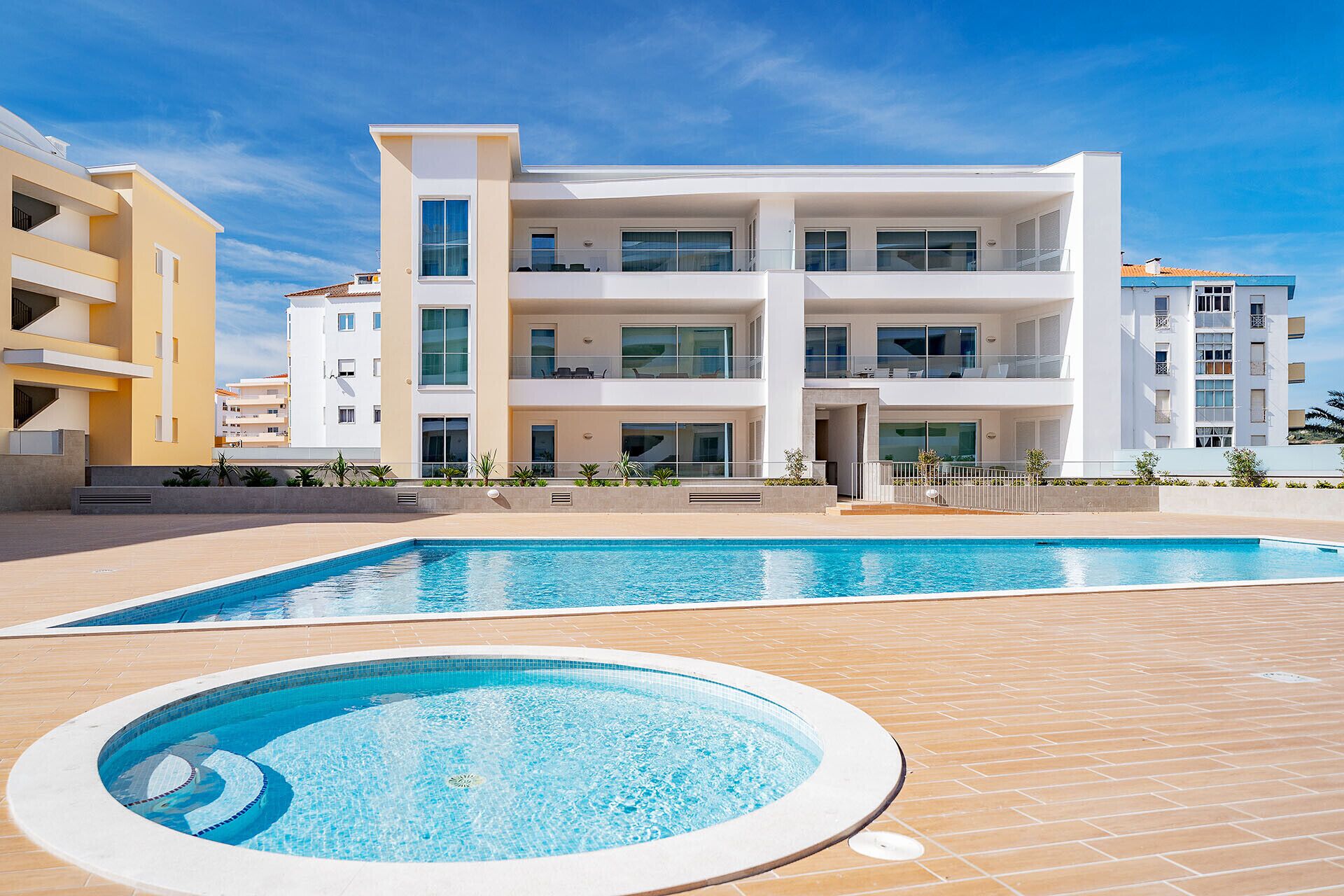 Un hôtel moderne à plusieurs étages, doté d’un espace piscine comprenant un jacuzzi et une piscine rectangulaire.