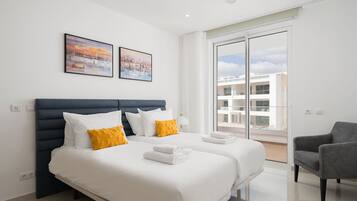 Une chambre d’hôtel moderne avec un grand lit, deux oreillers, une chaise et un balcon offrant une vue sur les immeubles.