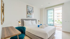 Une chambre d’hôtel moderne avec un grand lit, un bureau, un fauteuil de couleur turquoise et une vue sur le balcon extérieur.