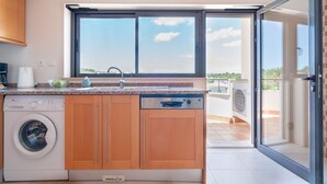 Una cuina compacta amb rentadora, un rentaplatets i una finestra amb vista a un balcó.