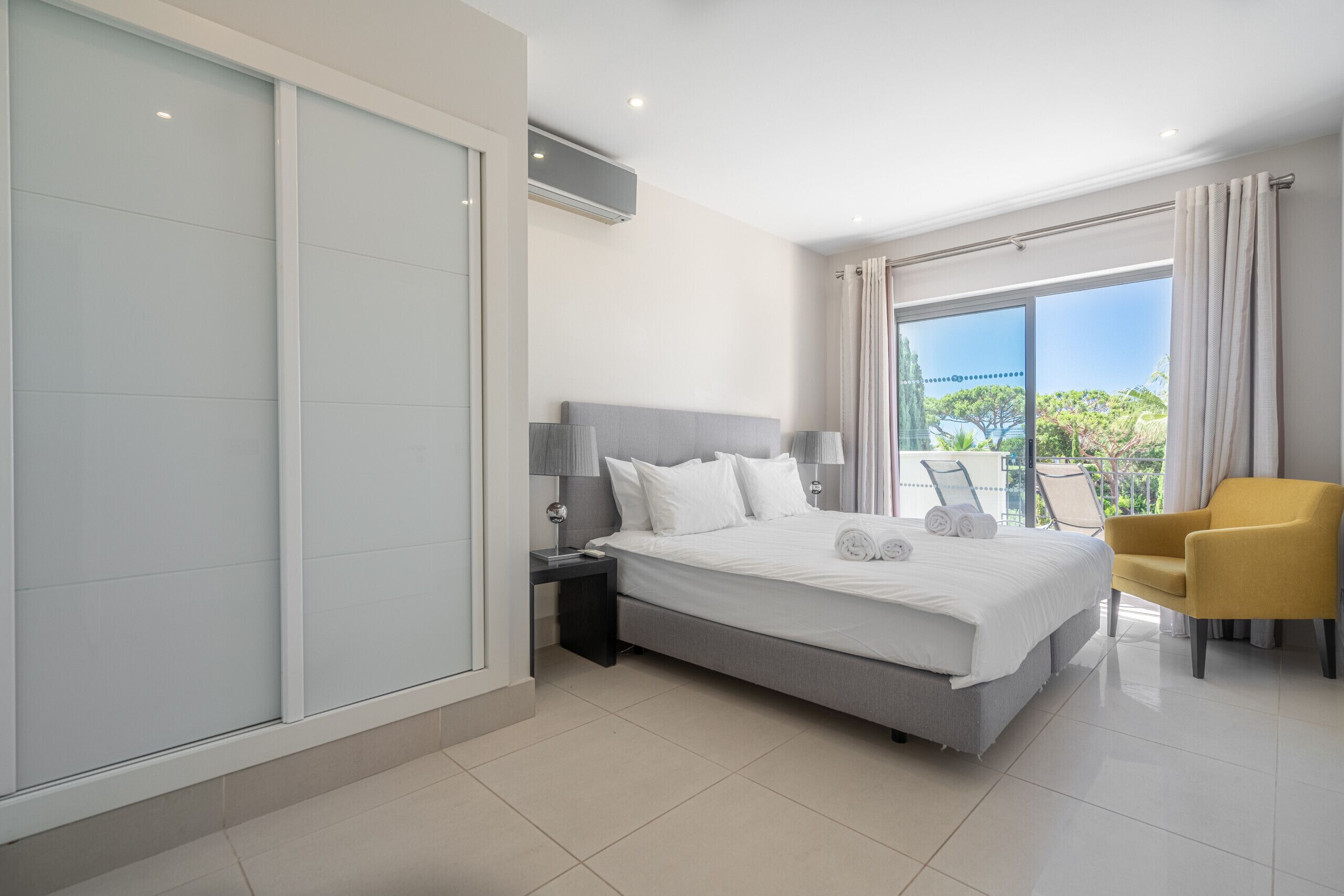 Una moderna camera d'hotel con un letto grande, un comodino, una sedia e una porta scorrevole in vetro che dà su un balcone.
