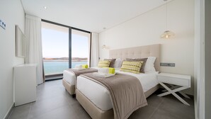 Quarto moderno com uma cama grande, uma mesinha de cabeceira e vista para o mar.
