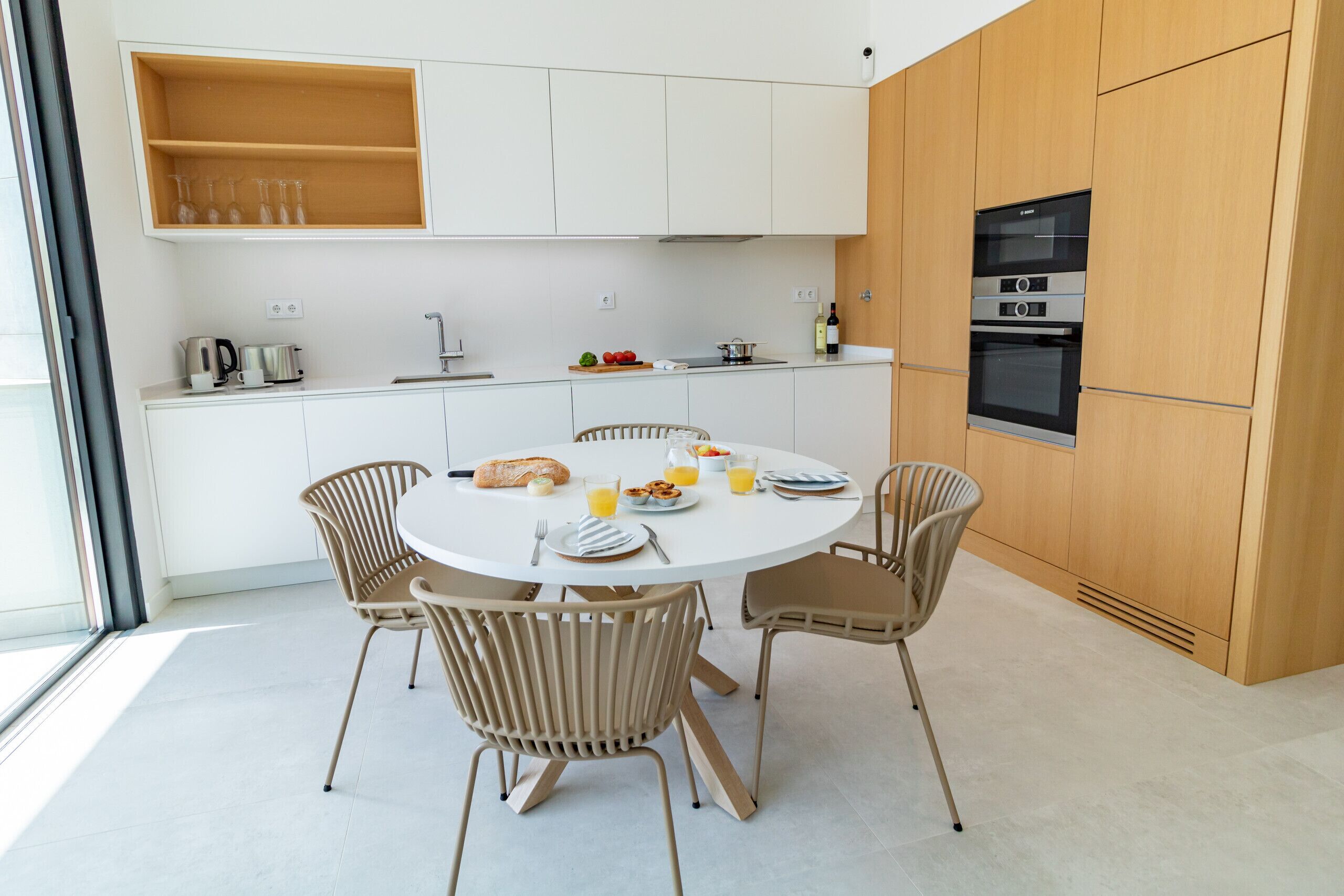 A modern kitchen with white cabinets, a built-in oven, and a dining area with a round table and four chairs.