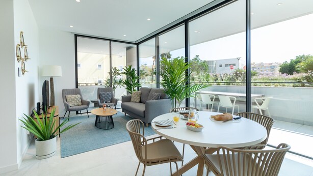 Ein modernes Wohnzimmer mit einem runden Esstisch, gemütlicher Sitzgelegenheit und großen Fenstern mit Stadtblick.