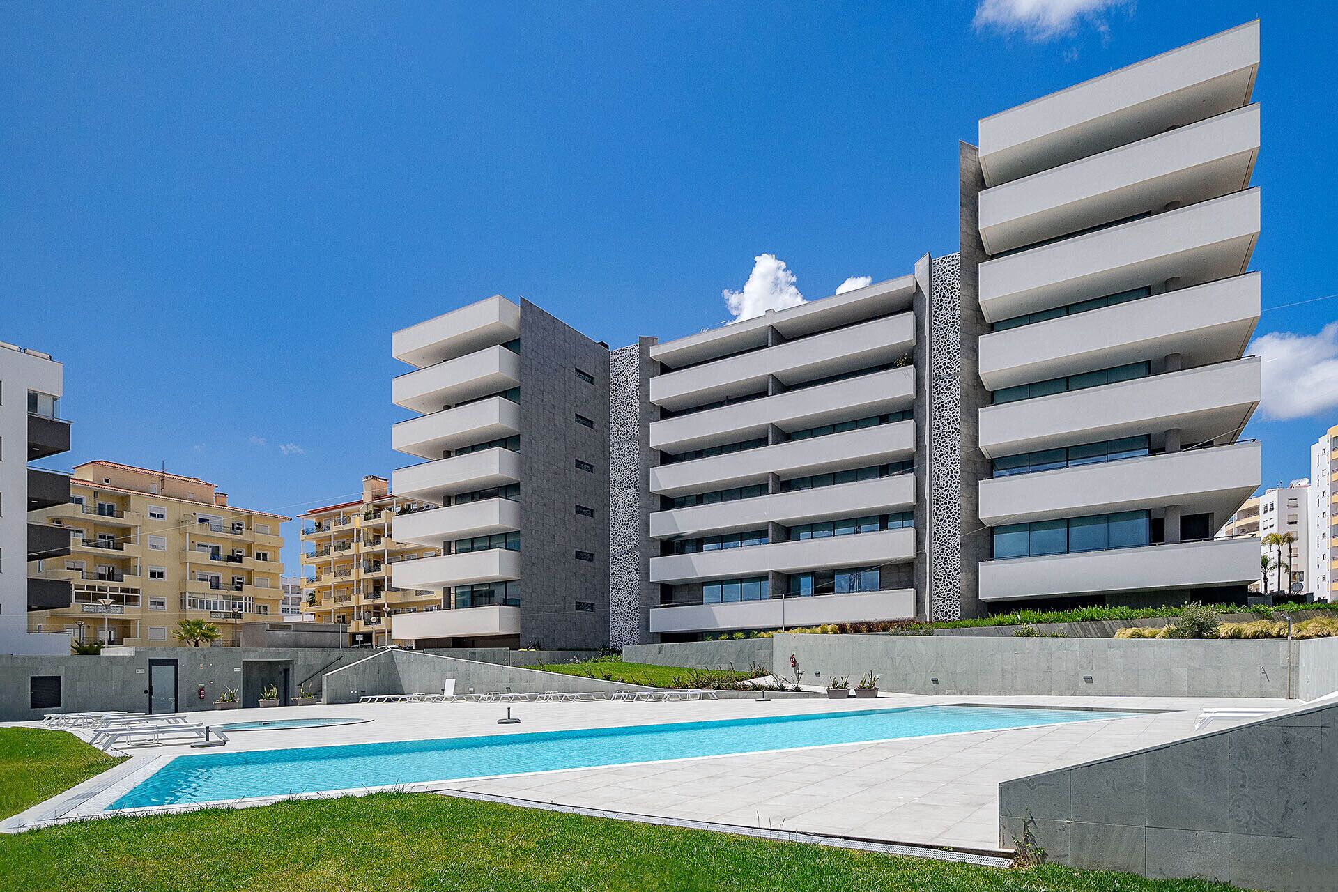 A modern apartment building with a swimming pool and a well-maintained lawn.
