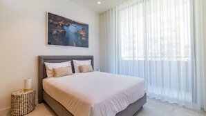 Ein modernes Schlafzimmer mit einem großen Bett, einem Nachttisch, einem Gemälde und transparenten Vorhängen.