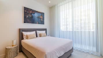 A modern bedroom with a large bed, a nightstand, a painting, and sheer curtains.