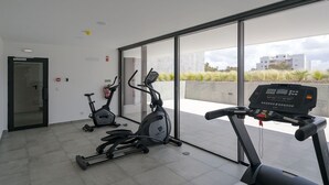 Ein modernes Fitnessstudio mit zwei Ergometer und einem Laufband, große Fenster mit Blick auf die Stadt.