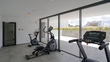 A modern gym with two stationary bikes and a treadmill, large windows offering a view of the city.