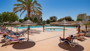 A poolside area with lounge chairs, umbrellas, and a palm tree. - PRAIA DA ROCHA OCEAN VIEW WITH POOL by HOMING (Portimão)