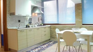 A compact kitchen with a sink, stove, and cabinets, a dining table with chairs, and a window with blinds. - Blue - Relaxation near Salerno, Pompeii &Amalfi (Pellezzano)