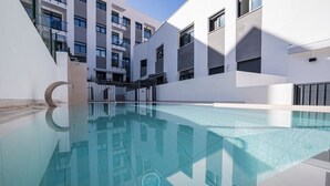 Een modern gebouw met een zwembad, balkons en een heldere lucht.
