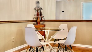 A dining area with a round glass table surrounded by four white chairs, a wooden ceiling, and a chandelier. - Charming 2-bedroom Townhouse in Kennesaw with Single Floor Layout (Kennesaw)