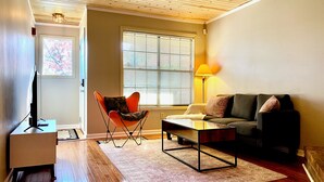 A living room with a wooden floor, a sofa, a chair, a coffee table, a TV, and a lamp. - Charming 2-bedroom Townhouse in Kennesaw with Single Floor Layout (Kennesaw)