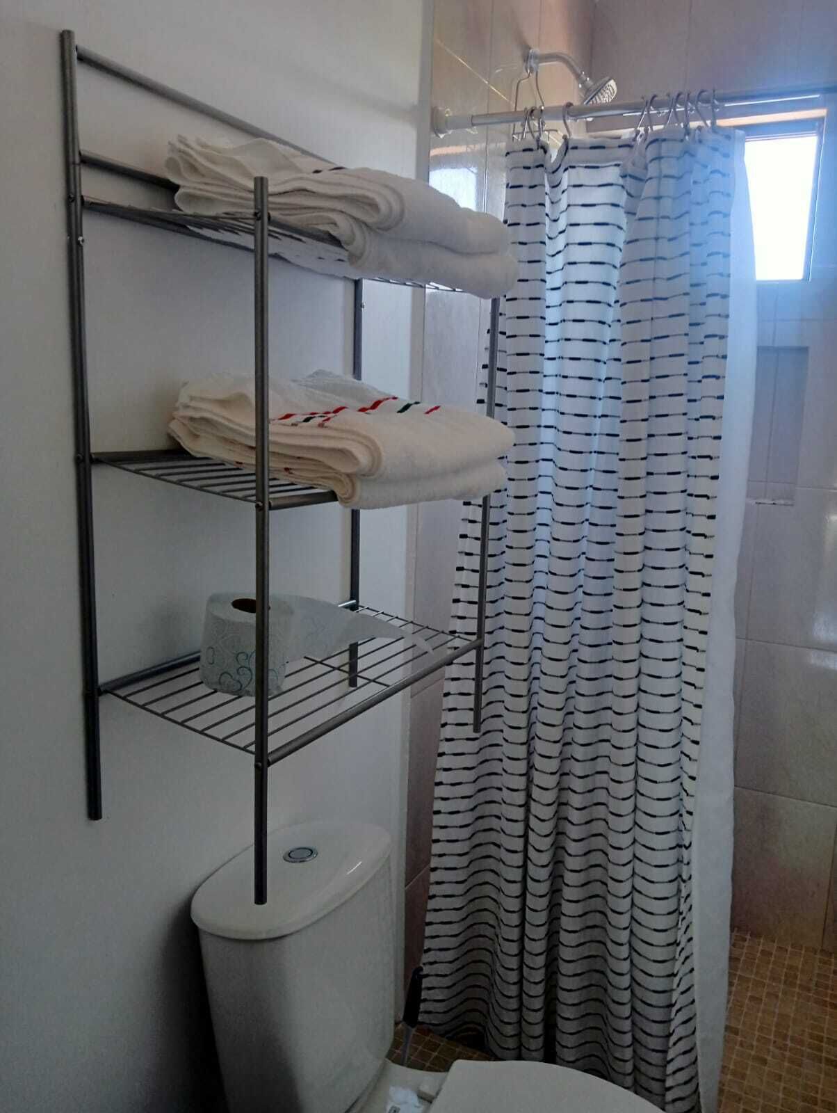 A bathroom with a metal shelf holding towels and toilet paper, a striped shower curtain, and a toilet.