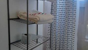 A bathroom with a metal shelf holding towels and toilet paper, a striped shower curtain, and a toilet.