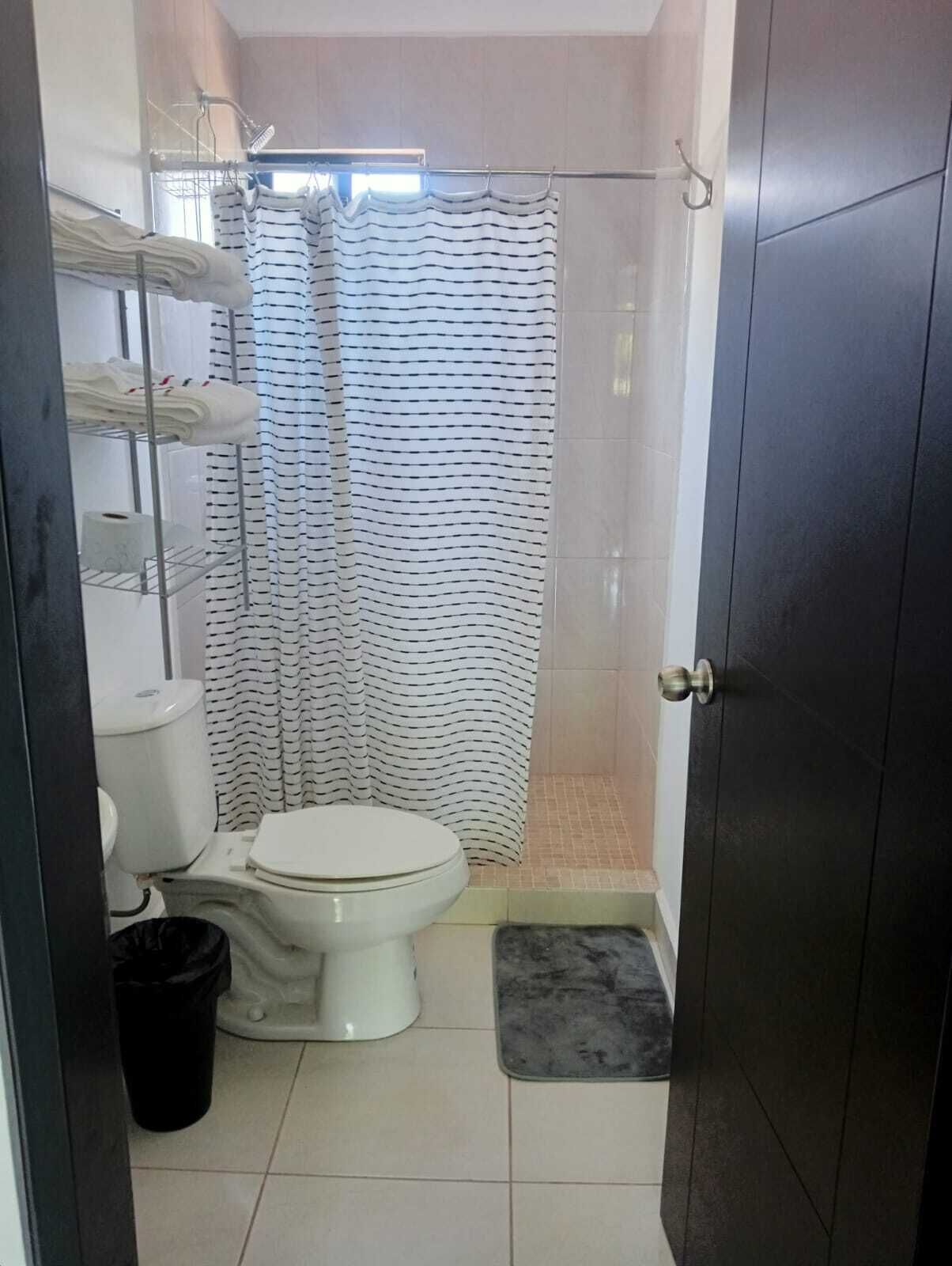 Un baño pequeño con inodoro, cortina de ducha, toallero y un cubo de basura.